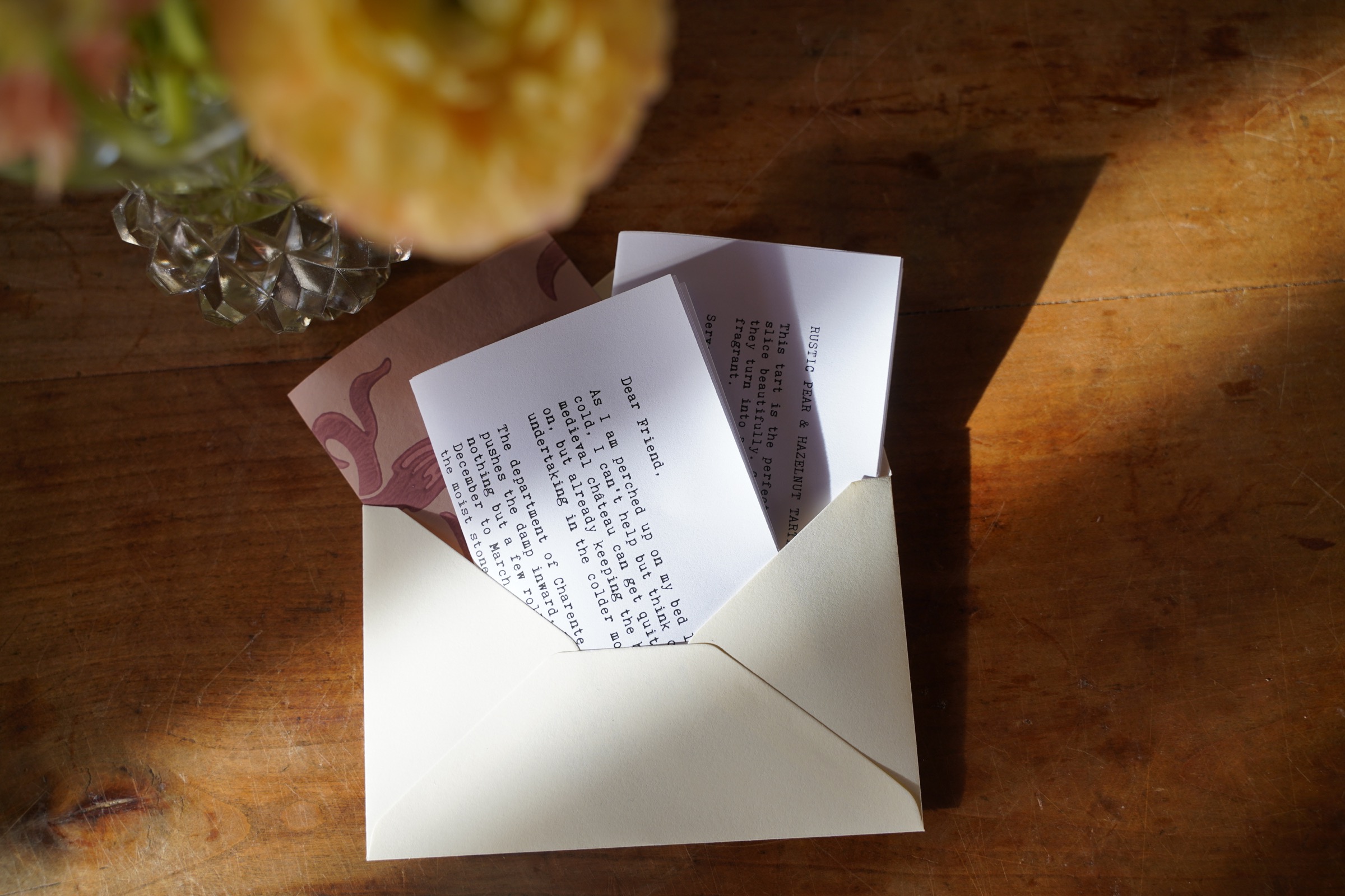 A Château Letter, recipe and seasonal printed pieces in warm sunlight on a wooden table
